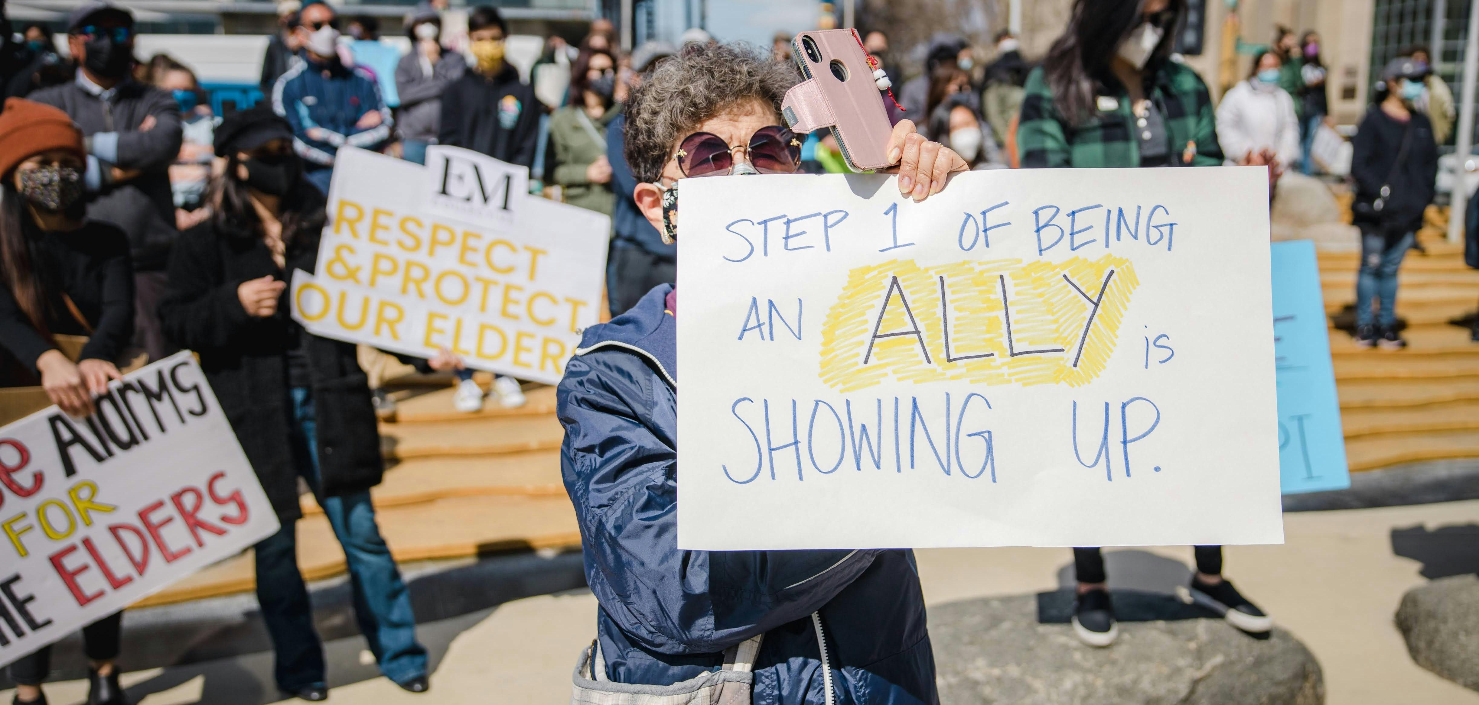 a person holding a sign that says "step 1 of being an ally is showing up."