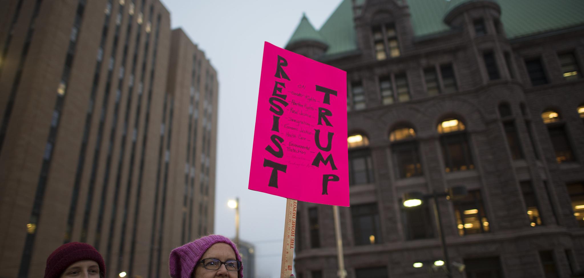 Woman holds a pink sign that reads "resist trump"