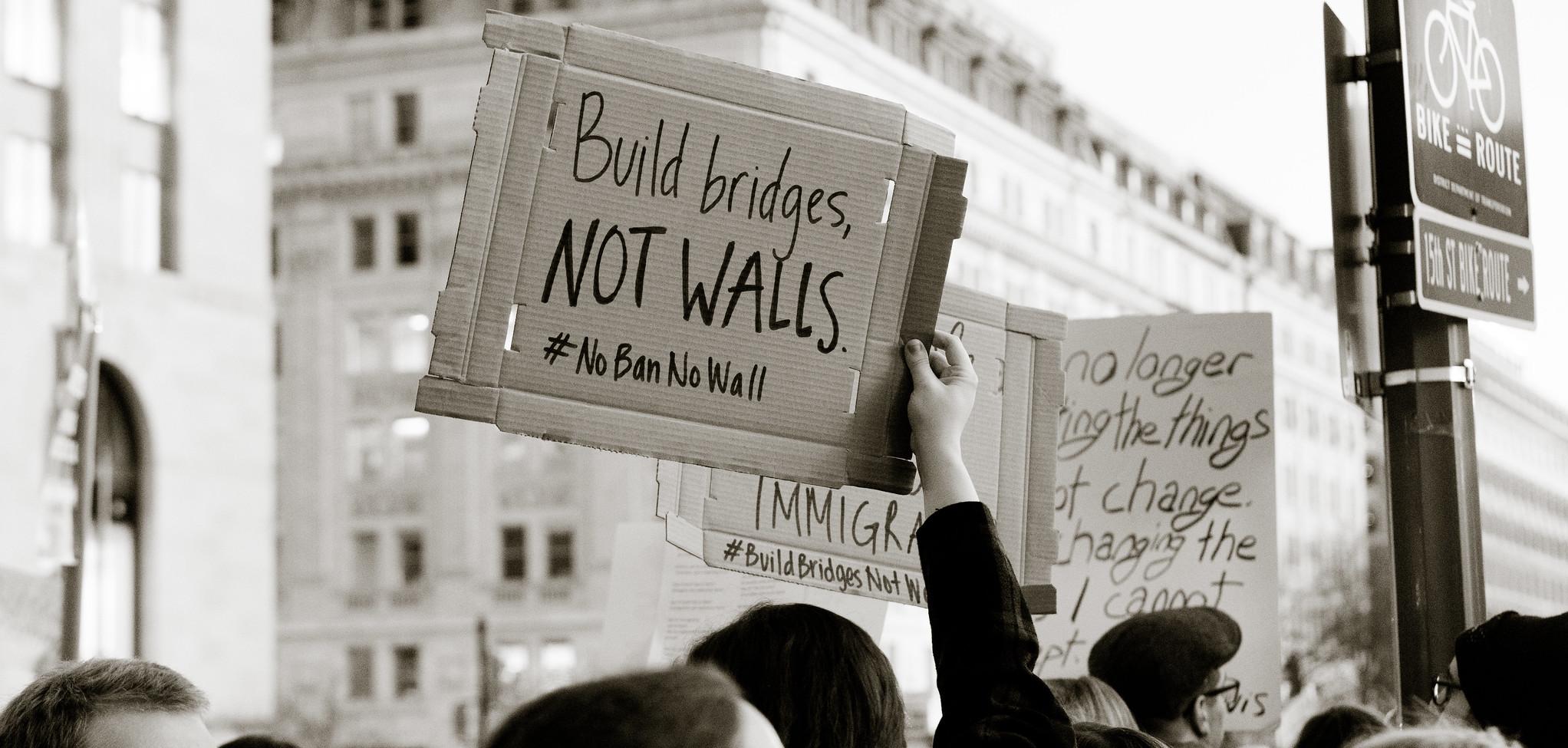 A protestor holding a sign that says "build bridges not walls"