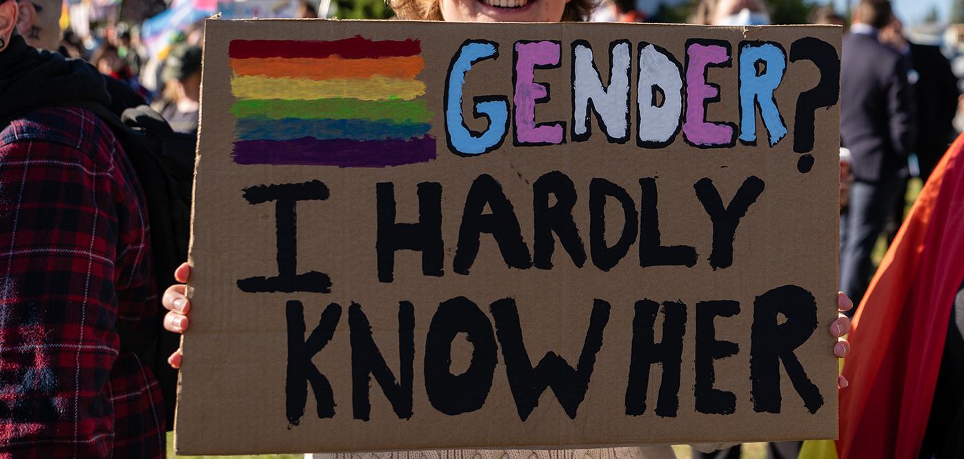 A sign at a protests saying "Gender? I hardly know her"