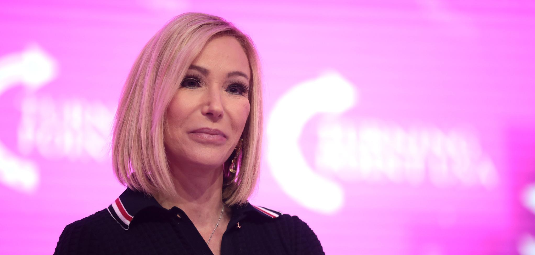 A woman in a black polo shirt with a pink background