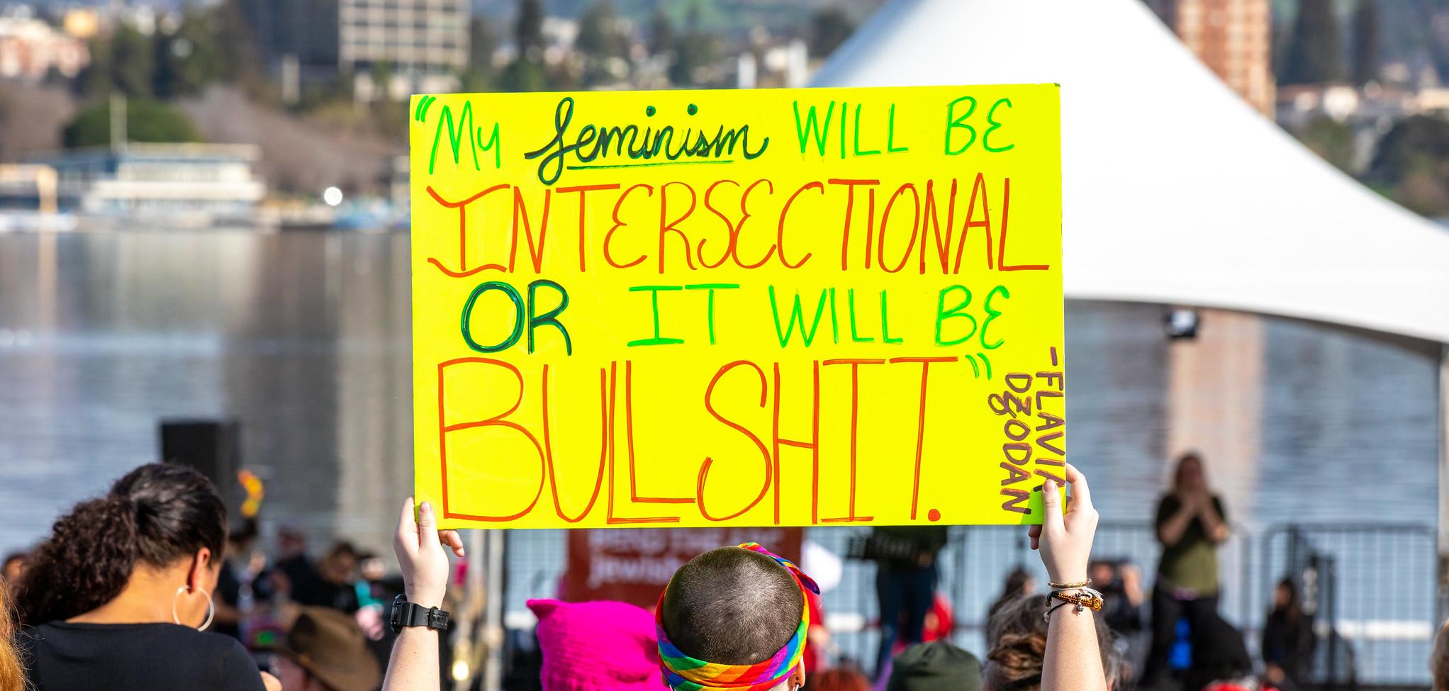 A person holding a yellow sign that reads "my feminism will be intersectional or it will be bullshit."