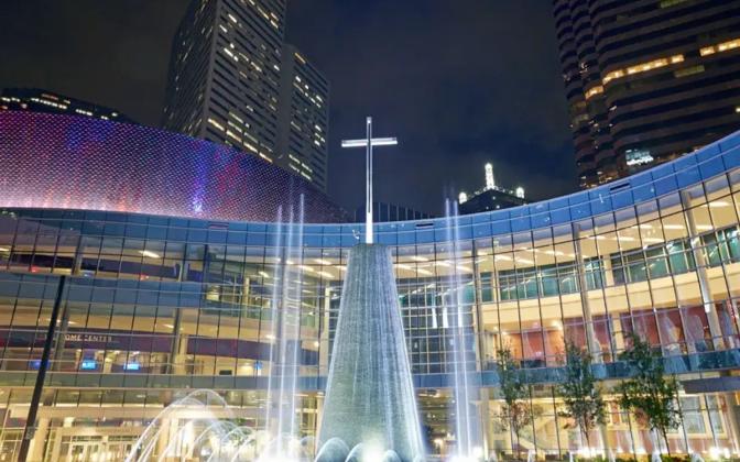 Modern, glass building with large cross sculpture in front surrounded by large fountain.
