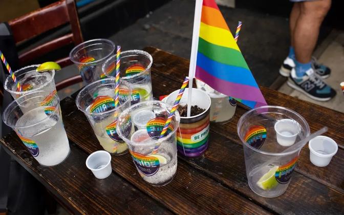 Plastic glasses with rainbow decals that say "Pride" on a table with remnants of drinks and a rainbow flag.