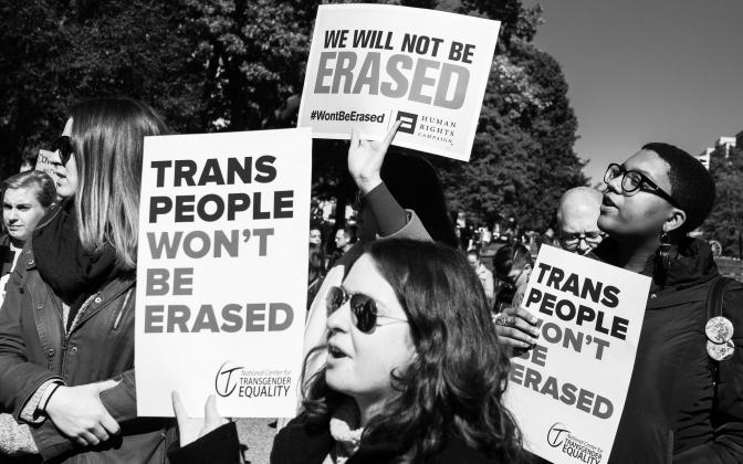 People at a protest holding signs that say "Trans people will not be erased" and "we will not be erased"