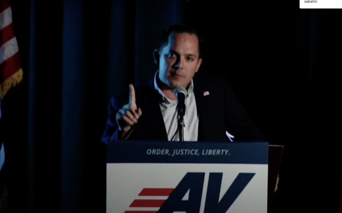 A man standing behind a podium with the American Virtue logo on it.