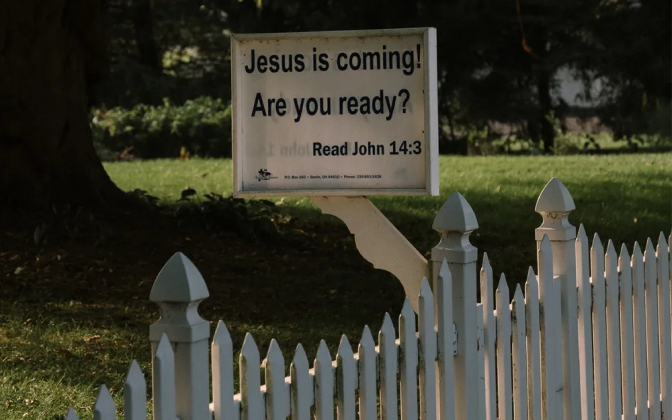 A sign post on a fence that reads "Jesus is coming! Are you ready?"