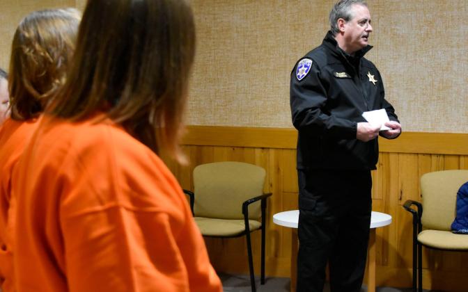 A man in a sheriff's outfit and a woman in an orange jumpsuit in the foreground.