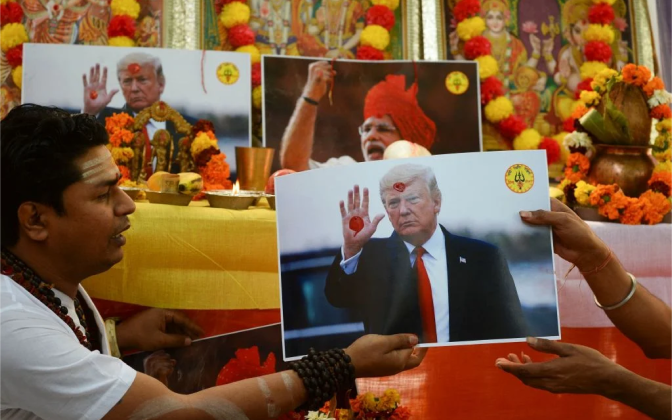 A man in religious outfit with a photo of Trump, performing a ceremony.